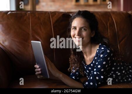 Happy woman relaxing on couch with tablet, holding device Stock Photo