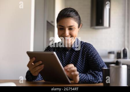 Happy Indian woman with tablet using app on computer Stock Photo