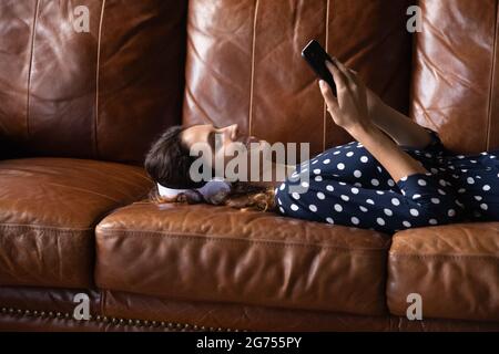 Happy calm Hispanic woman wearing headphones, resting on leather Stock Photo