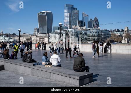 People enjoying some sunny weather socialising at The Scoop at More London and overlooking the cityscape and skyline of the City of London financial district on 17th April 2021 in London, United Kingdom. Stock Photo