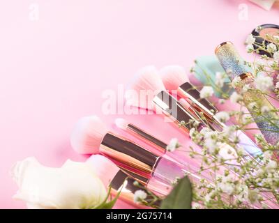 Trendy make up brushes with products on pink background with gypsophila flowers Stock Photo