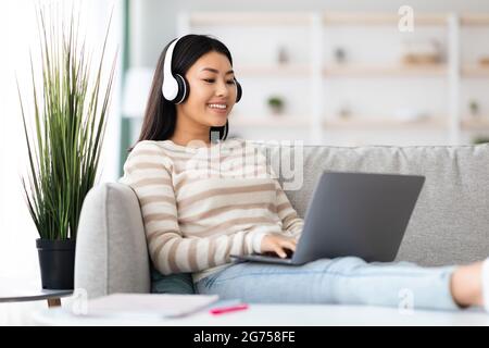 Young Asian Female Freelancer In Headphones Working Remotely With Laptop At Home Stock Photo