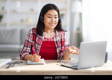 Distance Education. Young Asian Female Student Watching Webinar On Laptop At Home Stock Photo