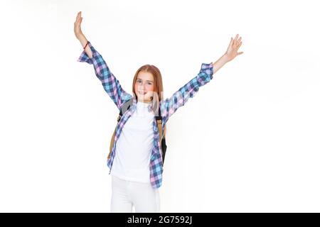 Teenager girl 11 years old schoolboy looking at the camera on a white background with a backpack and smiling holding up her hands high. Dressed in pla Stock Photo