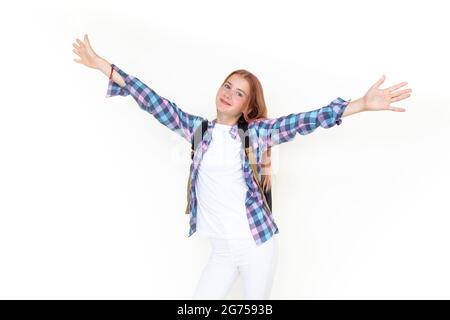 Teenager girl 11 years old schoolboy looking at the camera on a white background with a backpack and smiling holding up her hands high. Dressed in pla Stock Photo