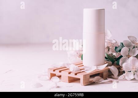 Antiperspirant roll-on deodorant on wooden podium in form of pallet on light plaster surface with apple flowers. Copy space Stock Photo