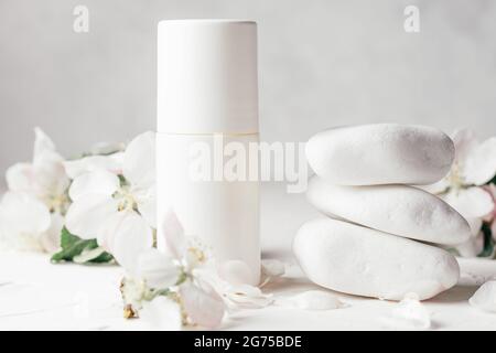 Antiperspirant roll-on deodorant near stack of white pebble stones on light plaster surface with apple flowers Stock Photo