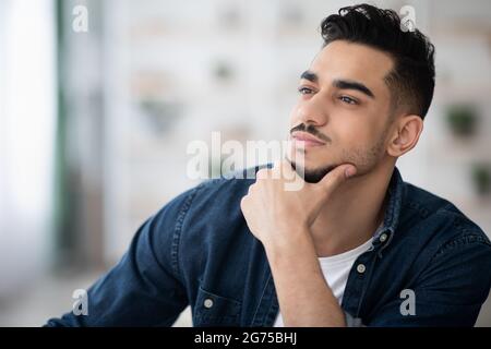 Pensive arab guy in casual sitting at workdesk, thinking Stock Photo