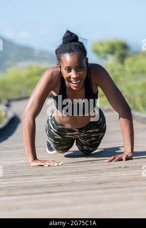 Struggling afro american woman doing push ups on a wooden runway: Exercise and effort concept. Stock Photo