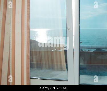 Curtains on the window, sea view at sunset, silver path, summer evening. Stock Photo