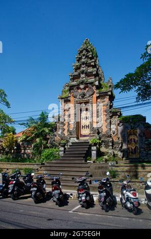 Motorbikes parked on the road by an ornate traditional doorway to property, Ubud, Bali, Indonesia Stock Photo