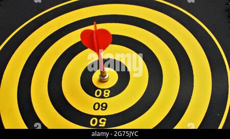 Red dart arrow hitting in the target center of dartboard with nice back ground. Business success concept shown with Dart and Dartboard. Marketing Aim Stock Photo