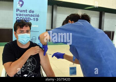 A health worker administers the first dose Comirnaty (PfizerBioNTech) COVID-19 mRNA Vaccine to a man at the Calafell Vaccination Center. The Department of Health of Catalonia through the Xarxa Santa Tecla de Tarragona in prevention against the contagion of SARS-CoV-2 Covid-19 has administered the first dose of the COMIRNATY vaccine (COVID-19 mRNA vaccine, Pfizer-BioNTech) to people between the ages of 16 and 34 at the vaccination center located at the Joan Ortoll Sports Pavilion in Calafell. (Photo by Ramon Costa / SOPA Images/Sipa USA) Stock Photo