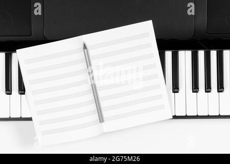 Music learning background. Piano keyboard and open blank sheet music notebook. Top view Stock Photo