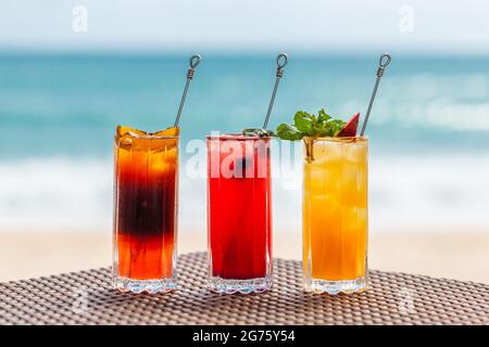 Set of Refreshing Fruit Cocktails Standing on Table on Beach near Turquoise Sea Stock Photo