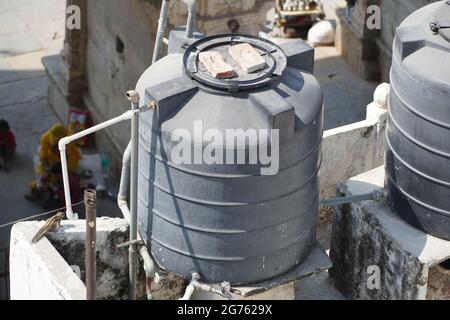 Polyvinyl chloride PVC water pipes connected to unidentified overhead tank. Black water tanks of industrial building on roof top or deck. - Mumbai Ind Stock Photo