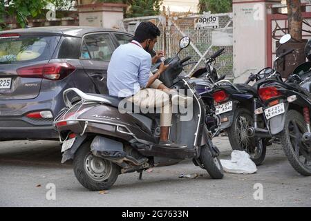 A Man casually sitting on his motorcycle and looking at phone outside a building. : Udaipur India - August 2020 0RM3 Stock Photo