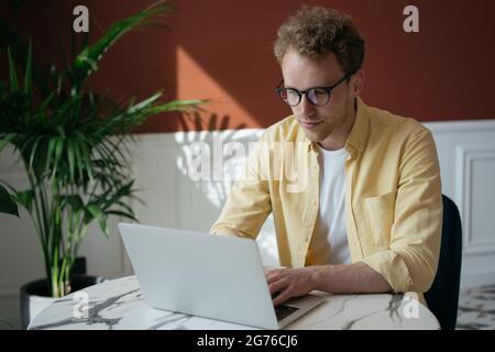 Successful freelancer copywriter working from home. Pensive man using laptop computer typing on keyboard, watching online training courses Stock Photo