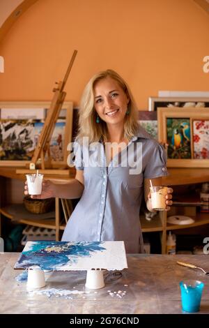 Beautiful artist in her studio shows process of creating picture. Interior painting. Happiness and creativity. Hobbies and crafts. Work of art Stock Photo