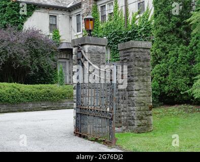 open gate to an old estate house, now rusty and falling off its hinges Stock Photo