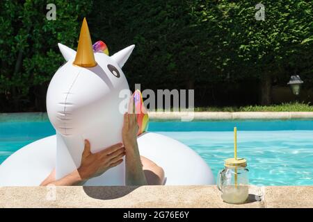 Young man hands touching a unicorn inflatable ring in a swimming pool. Summer concept. Stock Photo
