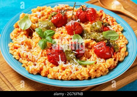 creamy tomato risotto with cherry tomatoes and sauce pesto on a blue plate, close-up Stock Photo