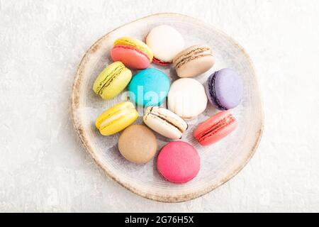 Multicolored macaroons on ceramic plate on gray concrete background. top view, close up, still life. Breakfast, morning, concept. Stock Photo