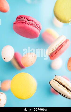Multicolored flying macaroons and chocolate eggs frozen in the air on blurred blue background. top view, flat lay, close up. Breakfast, morning, conce Stock Photo