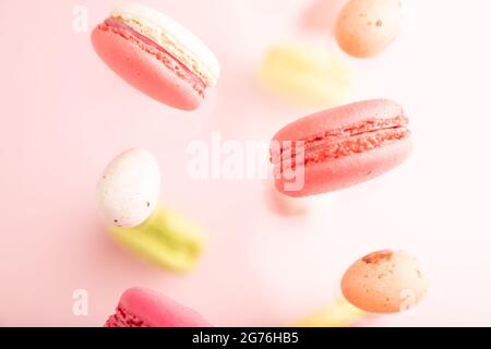 Multicolored flying macaroons and chocolate eggs frozen in the air on blurred pink background. top view, flat lay, close up. Breakfast, morning, conce Stock Photo