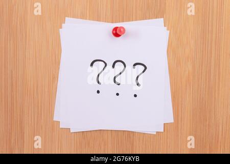 White Sticky Notes with Three Question Marks Pinned to the Wooden Message Board. To Do List Reminder in the Office. Memo Note at Work Stock Photo