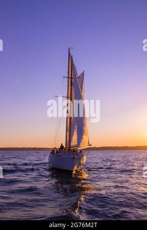 Newport, Rhode Island - July 29, 2020:  Sailboat sails beneath a colorful sunset sky along the coast of Newport Rhode Island Stock Photo