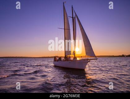 Newport, Rhode Island - July 29, 2020:  Sailboat sails beneath a colorful sunset sky along the coast of Newport Rhode Island Stock Photo