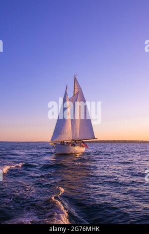 Newport, Rhode Island - July 29, 2020:  Sailboat sails beneath a colorful sunset sky along the coast of Newport Rhode Island Stock Photo