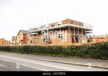 New build house half erected with scaffolding and safety boards around it on a new housing development site Stock Photo