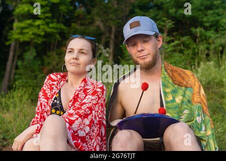 Perm Krai, Russia - June 27, 2021: couple of young people sitting outdoors, a man playing on a hank drum Stock Photo