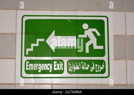 Emergency Fire Exit sign in corridor point way out of the building to escape in case of emergency, urgency and fire, Translated Arabic words ( exit in Stock Photo