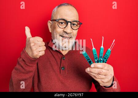 Handsome mature man holding picklock to unlock security door smiling happy and positive, thumb up doing excellent and approval sign Stock Photo