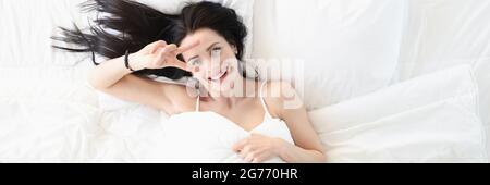 Portrait of smiling young woman on white bed making hand gesture Stock Photo