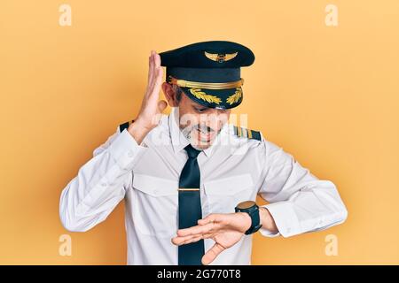 Handsome middle age man with grey hair wearing airplane pilot uniform looking at the watch time worried, afraid of getting late Stock Photo
