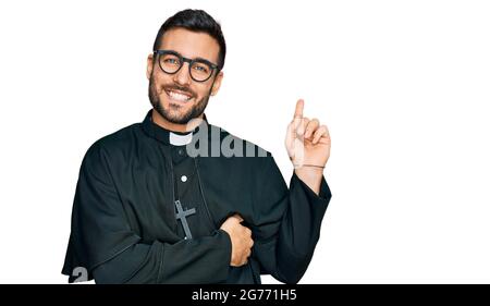 Young hispanic man wearing priest uniform smiling happy pointing with hand and finger to the side Stock Photo