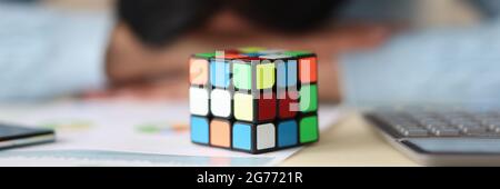 Rubik is cube on table with tired woman in background Stock Photo
