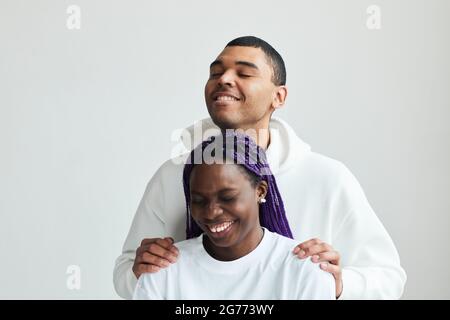Minimal vertical portrait of young mixed-race couple wearing white laughing while posing in studio Stock Photo