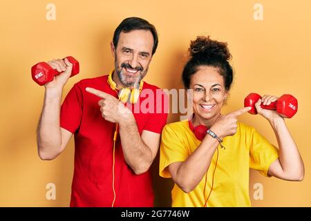 Middle age couple of hispanic woman and man wearing sportswear using dumbbells smiling happy pointing with hand and finger Stock Photo