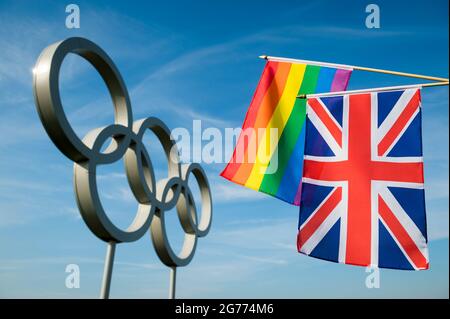 RIO DE JANEIRO - MAY 4, 2016: A rainbow colored gay pride flag hangs together with a British Union Jack in front of Olympic Rings against bright blue Stock Photo