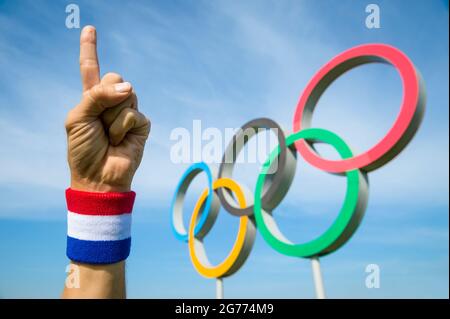 RIO DE JANEIRO - CIRCA MAY, 2016: A hand wearing red white and blue wristband makes a number sign in front of Olympic Rings Stock Photo