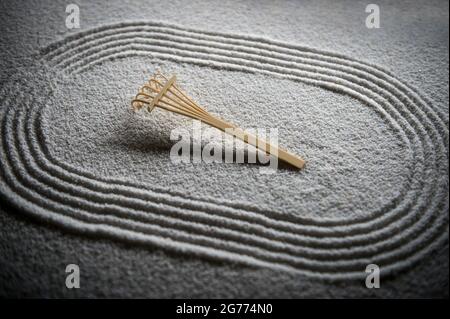 Wooden rake sits on Japanese Zen garden raked with a simple sports running track oval in textured white sand Stock Photo