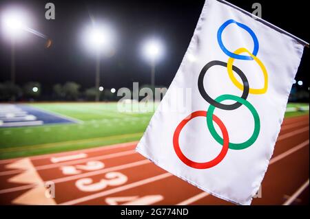 MIAMI, USA - AUGUST 15, 2019: An Olympic  flag waves under the floodlights of a red athletics track. Stock Photo