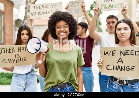 Group of young friends protesting and giving slogans at the street looking positive and happy standing and smiling with a confident smile showing teet Stock Photo