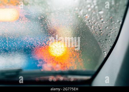 A selective focus shot of a windshield from inside a car with raindrops on it and orange bokeh lights behind it Stock Photo