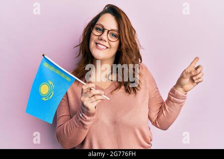 Young caucasian woman holding kazakhstan flag smiling happy pointing with hand and finger to the side Stock Photo
